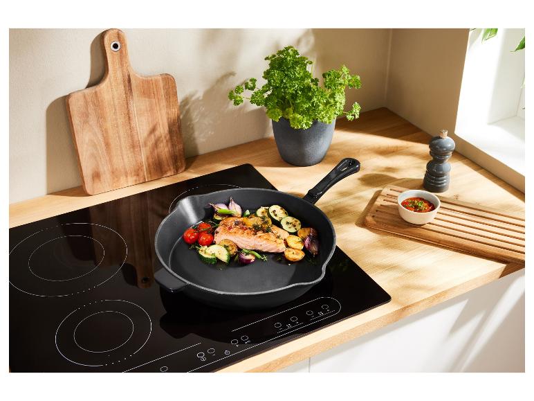 Une poêle noire avec du saumon et des légumes sur une plaque à induction.