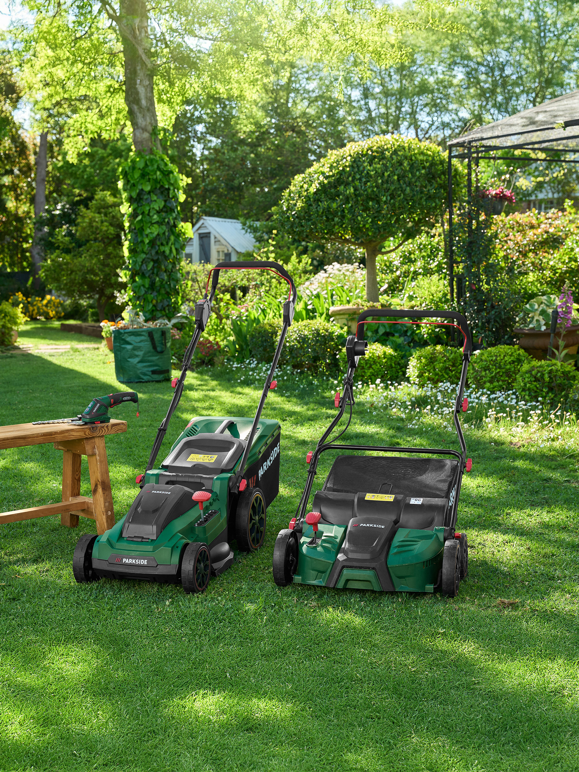 Deux tondeuses à gazon vertes Parkside et des outils de jardin sur une pelouse.