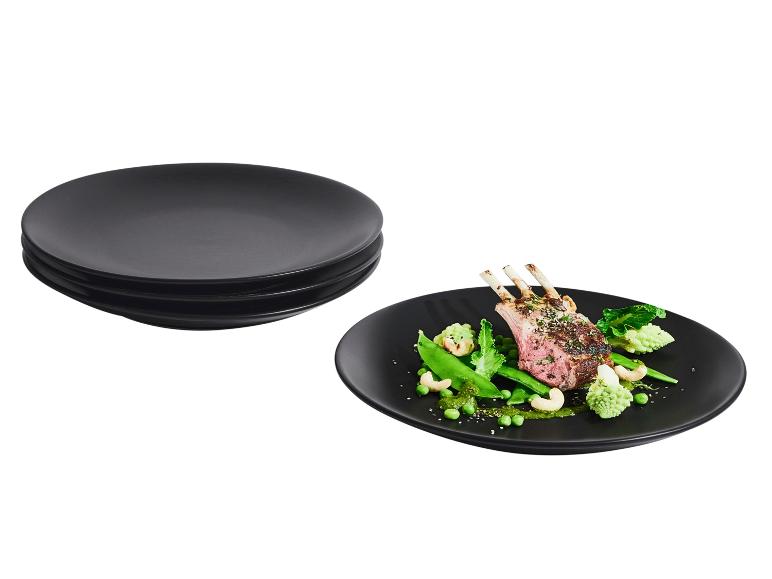 Assiettes noires empilées et une assiette noire avec des côtelettes d'agneau et des légumes.
