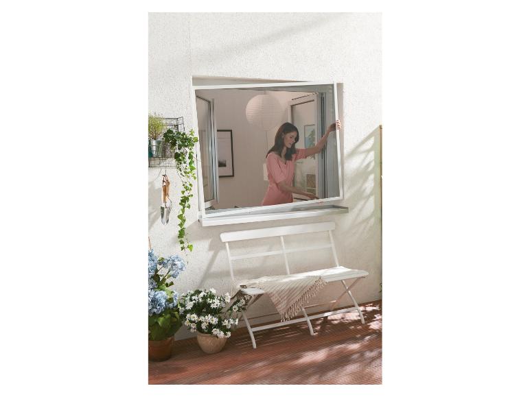 Une femme installe une moustiquaire sur une porte de terrasse.