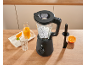 Mixeur noir avec glaçons, jus d'orange et tranches d'orange sur un comptoir en bois.