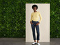 Une femme en haut jaune et un jean bleu pose devant un fond vert.