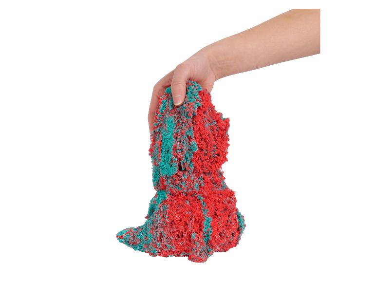 Une main tient un amas de sable cinétique rouge et turquoise.