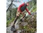 Une femme portant une veste rouge et un legging à fleurs marche sur un sentier de montagne.
