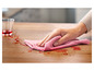Un chiffon rose est utilisé pour nettoyer une tache sur une table en bois.