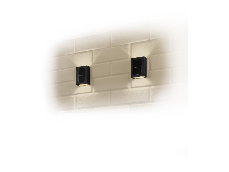 Deux appliques murales solaires noires rectangulaires sur un mur de briques blanches.
