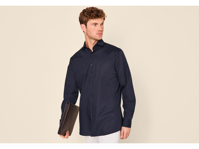 Homme portant une chemise à manches longues bleu marine, un pantalon blanc et un porte-documents marron.