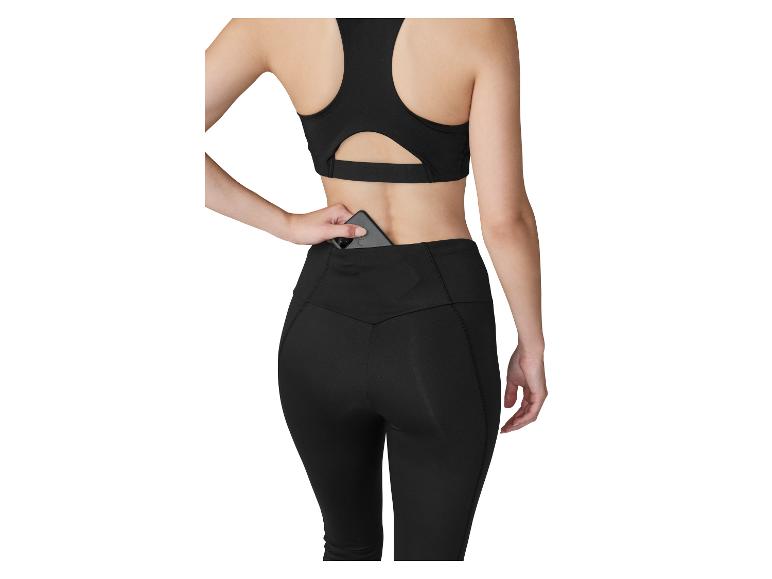 Femme en brassière de sport et legging noirs, rangeant un téléphone dans la poche arrière du legging.
