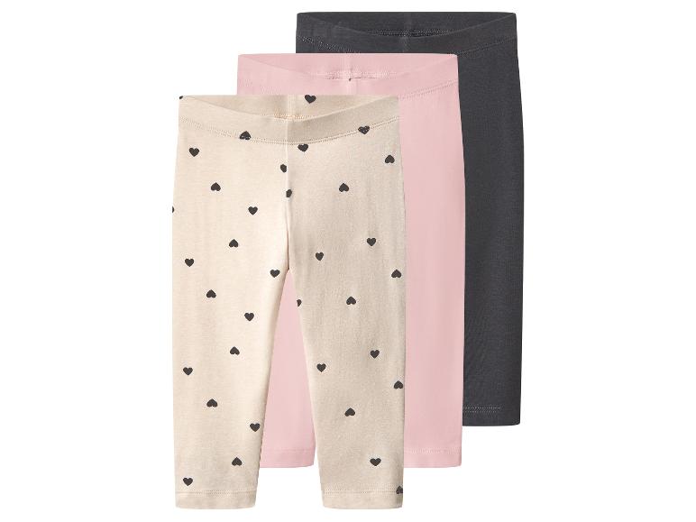 Trois leggings pour enfants : un beige à cœurs noirs, un rose et un gris foncé.
