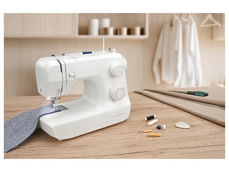 Machine à coudre avec tissu bleu, ciseaux et fils sur une table en bois.