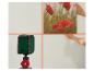 Un niveau laser projette des lignes croisées sur un mur, tandis que des mains placent un tableau de fleurs rouges.