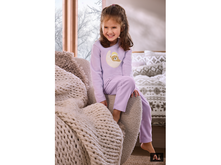 Fille en pyjama violet avec ourson, assise sur un fauteuil à côté d'une couverture tricotée.