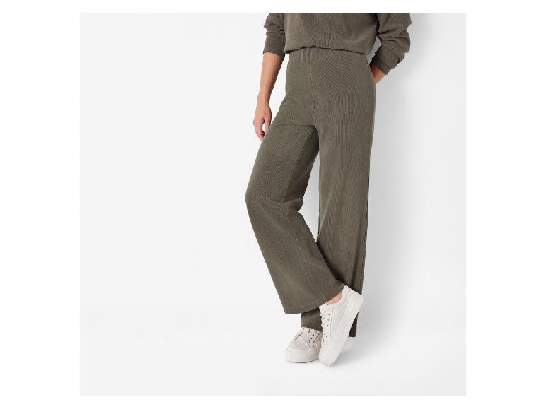 Un mannequin porte un pantalon en velours côtelé vert et des baskets blanches.