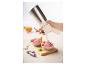Une main utilise un siphon de cuisine pour verser de la mousse rose dans des bols de fruits.