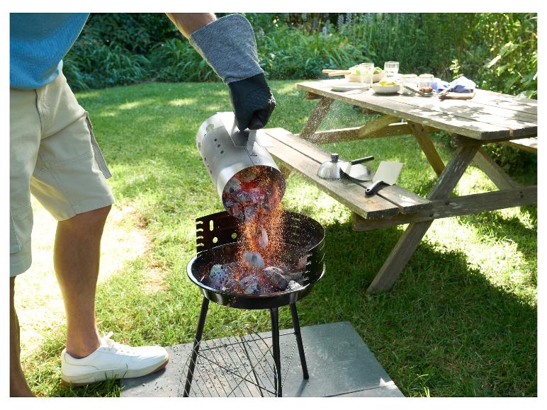 Homme versant des charbons ardents dans un barbecue au charbon de bois dans le jardin, table de pique-nique en arrière-plan.
