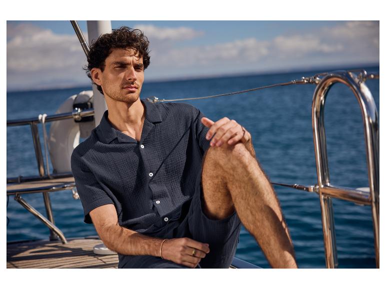 Un homme détendu en chemise et short foncés sur un yacht.