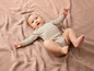 Un bébé dans un body rayé est couché sur une couverture rose.