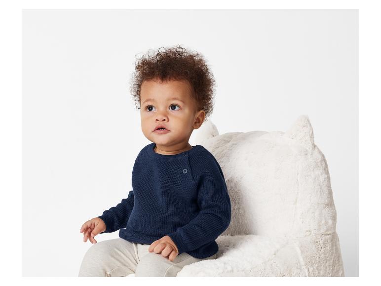 Bébé en pull bleu marine assis dans un fauteuil moelleux.