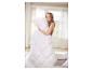 Femme souriante étreignant une couette et un oreiller blancs et moelleux dans une chambre lumineuse.