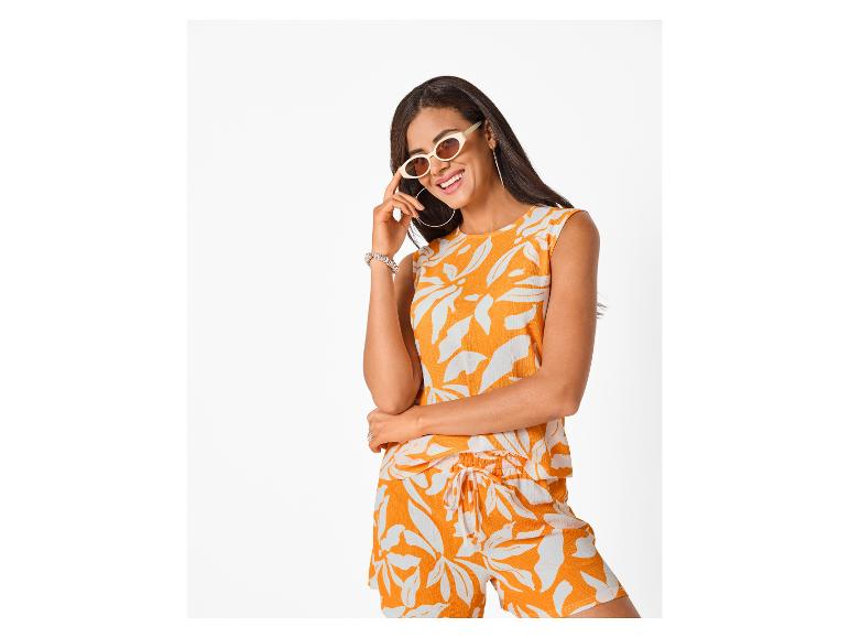 Femme en haut et short à motifs orange et blanc, portant des lunettes de soleil et des créoles.