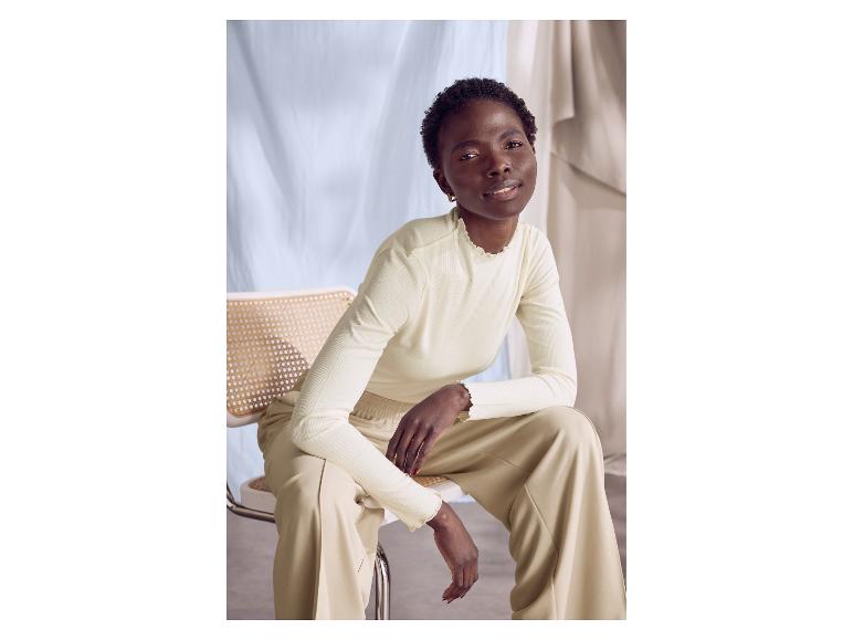 Femme assise sur une chaise, portant un haut à manches longues et un pantalon ample.