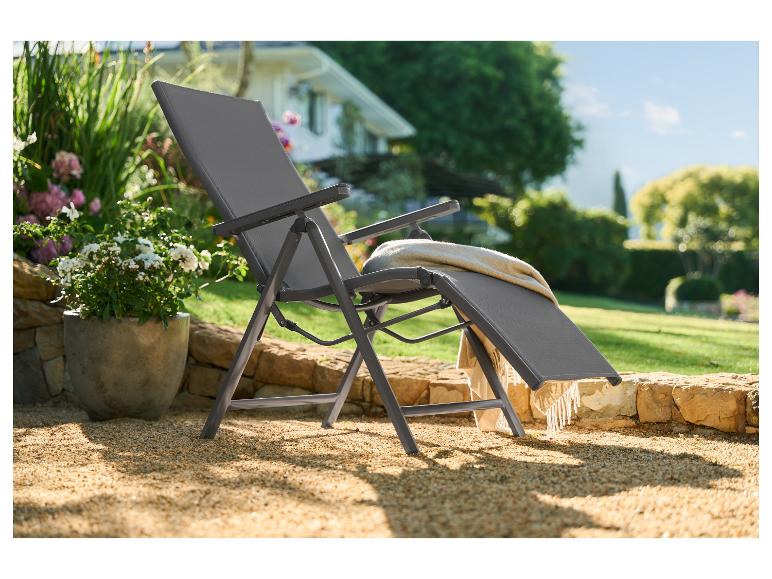 Chaise longue de jardin pliable avec couverture sur une cour de gravier avec fleurs et maison.