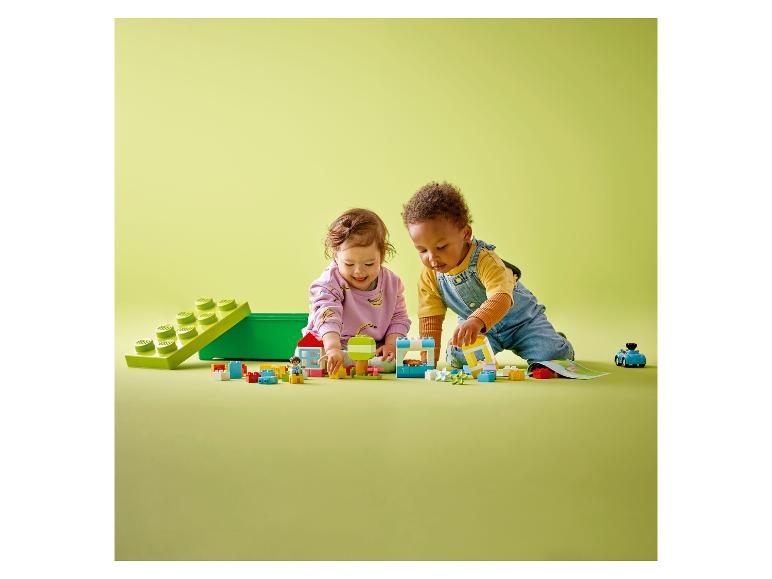 Deux tout-petits jouent avec des briques et des figurines LEGO DUPLO colorées sur une surface verte.