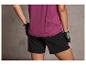 Une femme porte un t-shirt de sport violet et un short noir.
