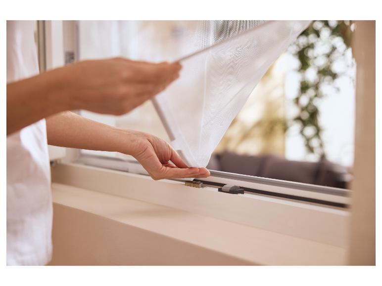 Personne installant une moustiquaire blanche sur une fenêtre.