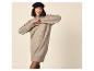 Femme souriante en robe pull tricotée beige et casquette noire.
