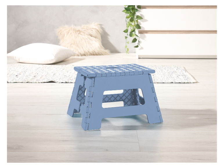 Tabouret pliable bleu clair à pois blancs sur un sol en bois.