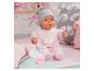 Poupée bébé en grenouillère rose avec bonnet, biberon et sucette sur un lit.
