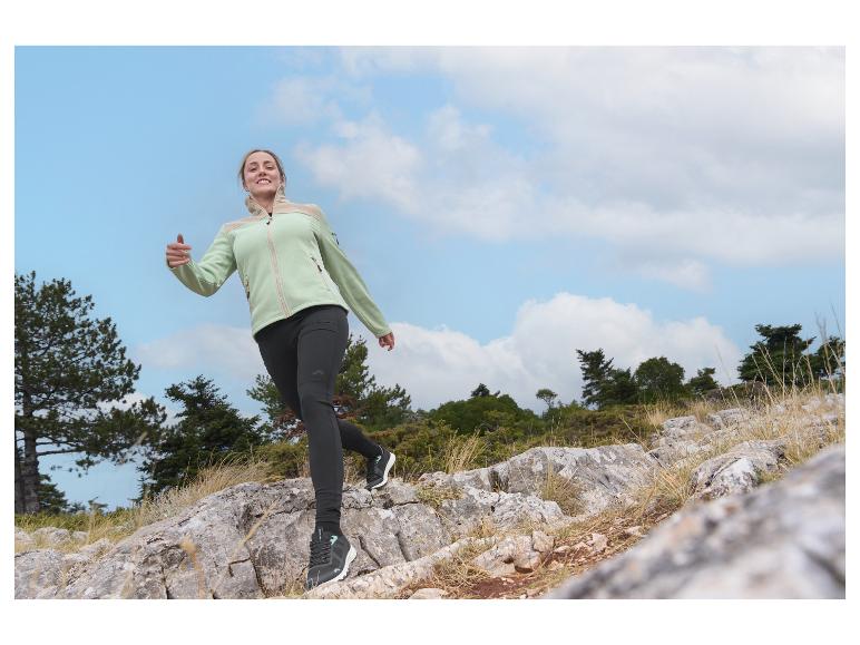 Femme en veste polaire vert clair et leggings foncés faisant de la randonnée sur un sentier rocheux.