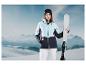 Une femme vêtue d'une veste de ski bleue et d'un pantalon blanc tient un ski dans un environnement montagneux enneigé.