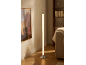 Lampadaire cylindrique avec base chromée éclairant un salon moderne avec étagère et canapé.