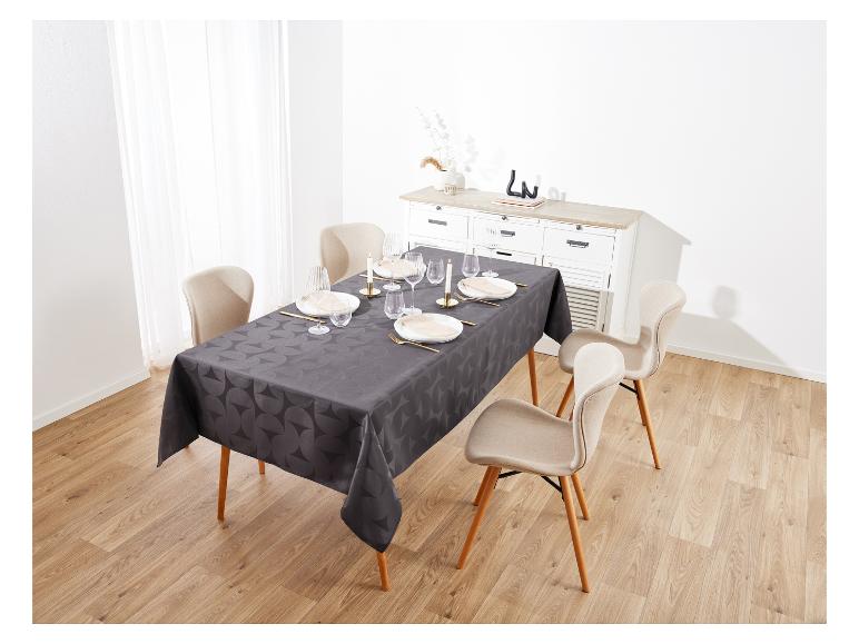 Une nappe noire à motifs géométriques habille une table à manger avec des chaises beige clair.