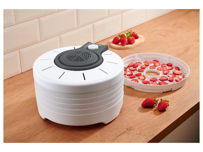 Déshydrateur alimentaire blanc avec des fraises fraîches et séchées dans une cuisine.