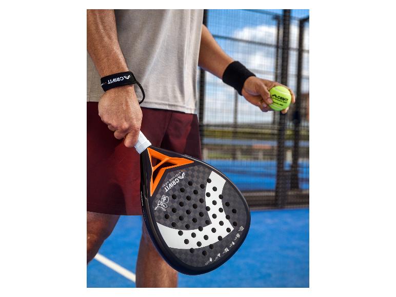 Raquette de padel et balle tenues par un joueur sur un court de padel.