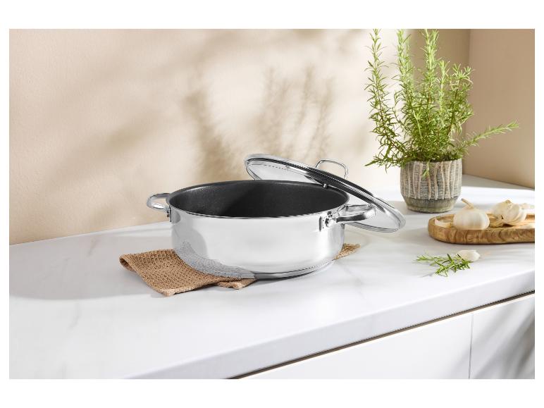 Marmite en acier inoxydable avec couvercle en verre sur un comptoir de cuisine blanc avec herbes et ail.