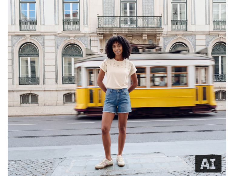 Femme en t-shirt beige ajouré et short en jean devant un tramway jaune.