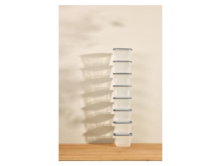 Une haute pile de récipients alimentaires en plastique transparent avec couvercles gris sur une surface en bois.