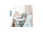 Chaise haute en bois vert clair avec harnais de sécurité, à côté d'une table blanche.