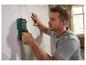 Homme utilisant un détecteur mural sur un mur tapissé.