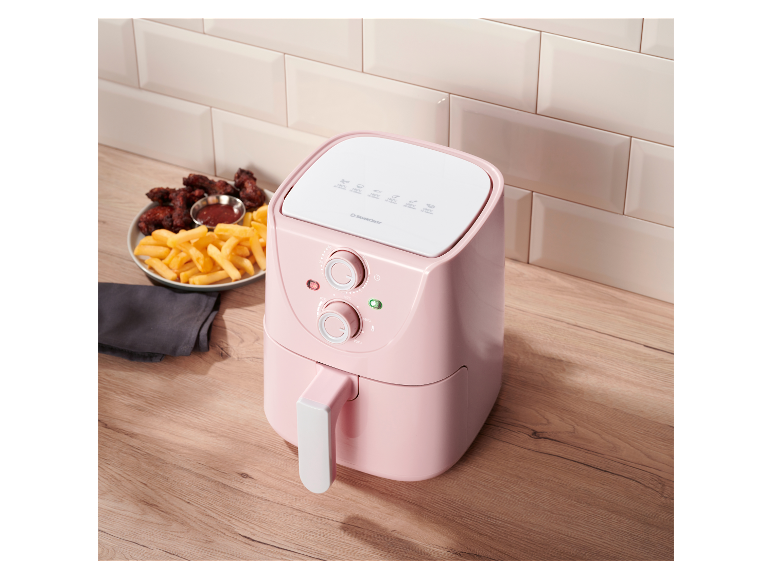 Une friteuse Silvercrest rose sur une table en bois à côté de frites et d'ailes de poulet.