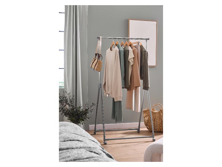 Portant à vêtements avec des vêtements de différentes couleurs, un sac et un panier dans une pièce.