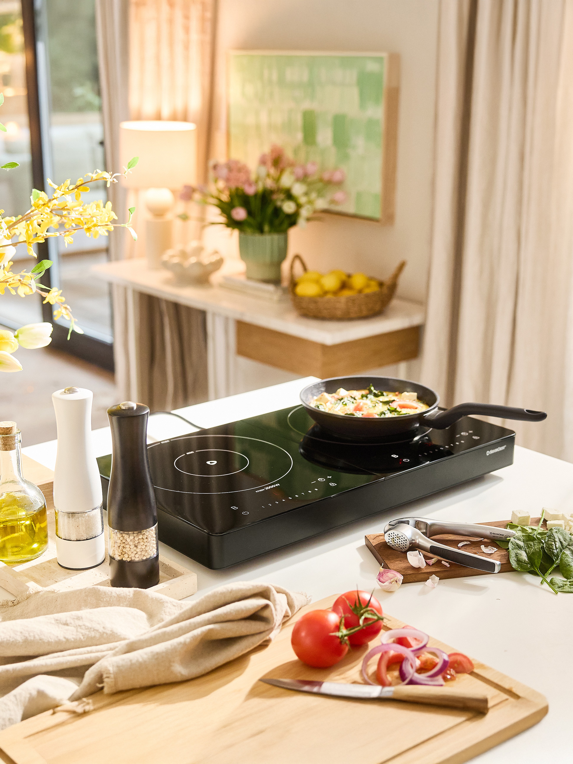 Plaque à induction SilverCrest avec poêle, épices et légumes frais sur un comptoir de cuisine.