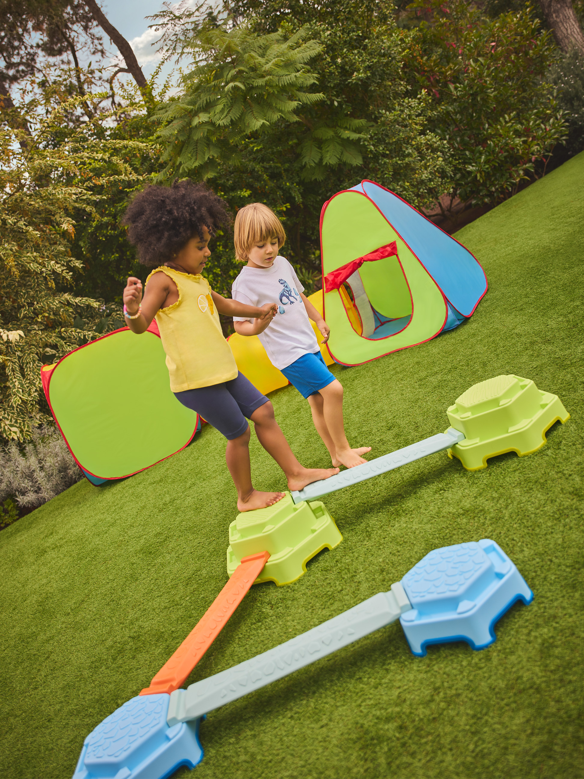 Deux enfants jouent sur une poutre d'équilibre colorée avec des tentes de jeu en arrière-plan.