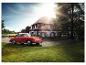 Une Porsche 911 rouge devant une maison avec un ciel ensoleillé.