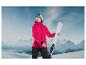 Une femme en veste de ski rose et masque de ski tient des skis blancs dans les montagnes.