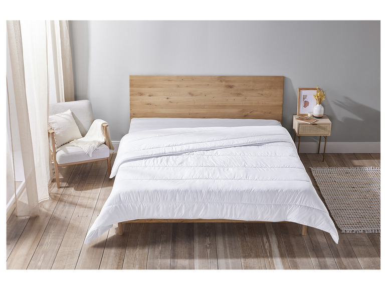 Une couette blanche sur un cadre de lit en bois dans une chambre à coucher.